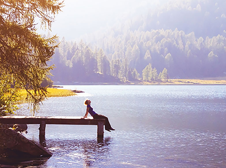 Person bathing in sunlight sitting on lake pier