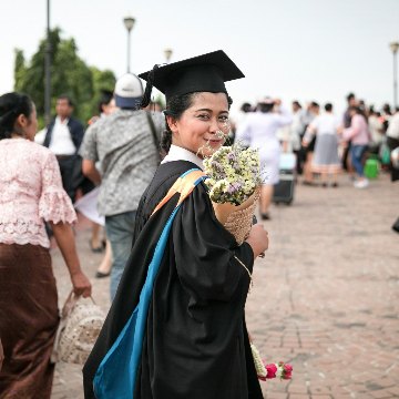 Happy graduate in academic dress holding bouquet