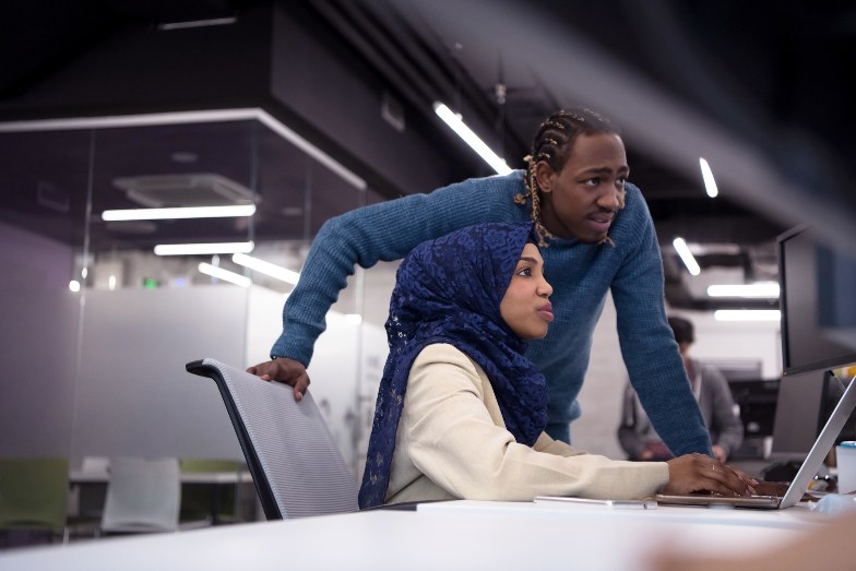 Student wearing hijab and teacher working together on laptop