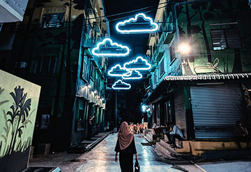 person walking down city street with neon cloud string lights above