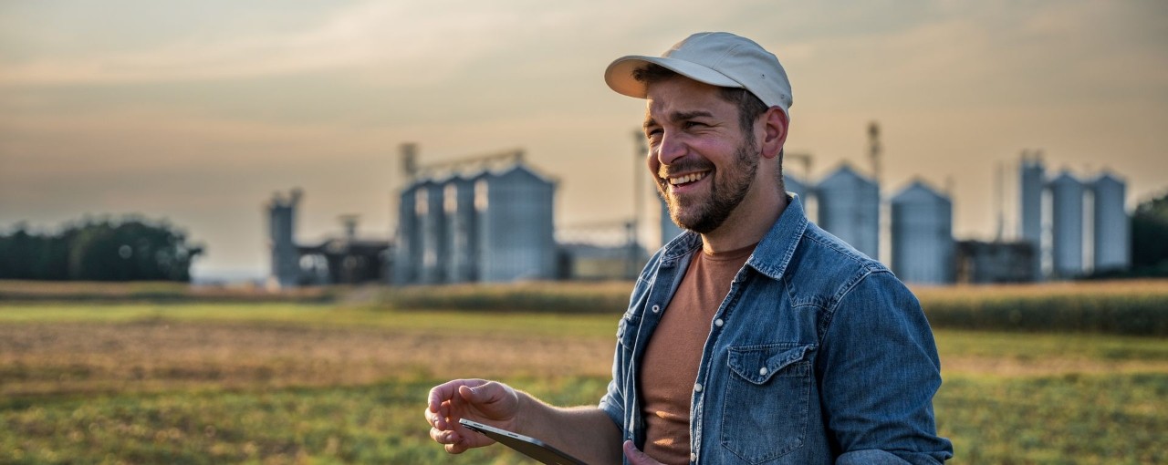 smiling person wearing cap in field with tablet