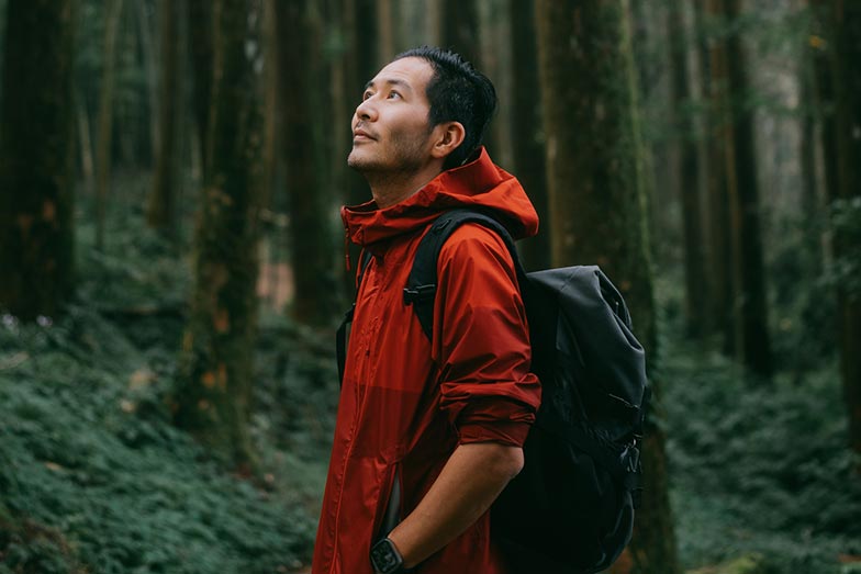 man in red shirt in the woods looking up