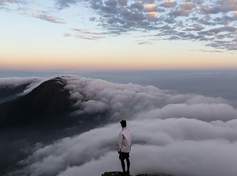 person standing at the top of mountain looking over clouds
