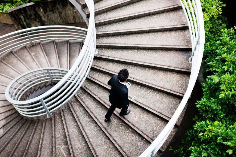 business person climbing external spiral staircase surrounded by green bushes